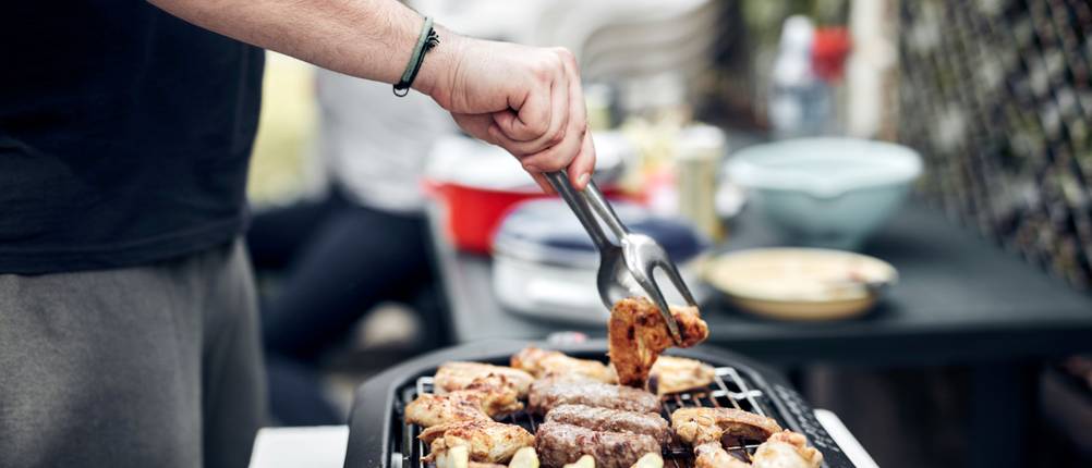 Mann wendet Grillfleisch auf dem Elektrogrill mit einer Grillzange.