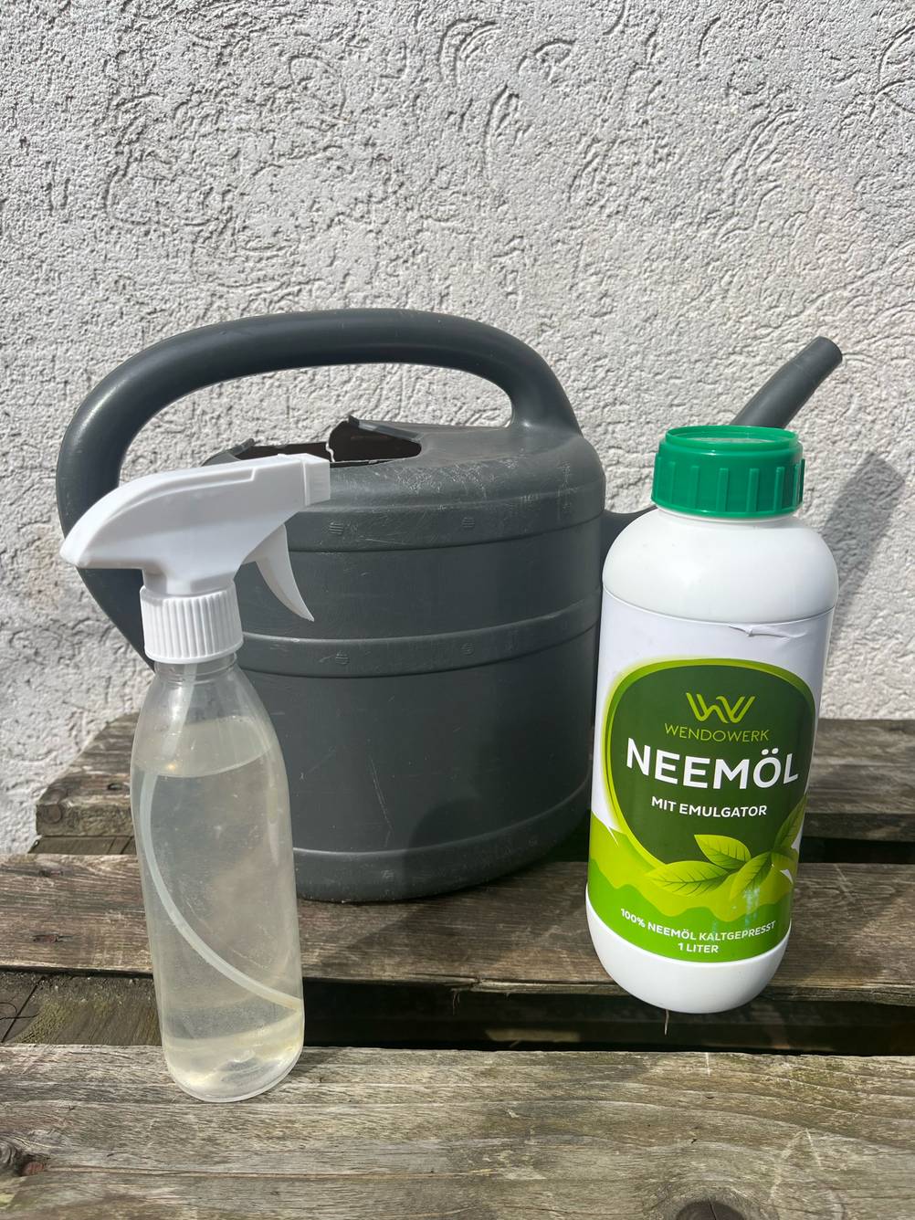 Eine Flasche Neemöl steht zum Testen neben einer Sprühflasche und vor einer Gießkanne.