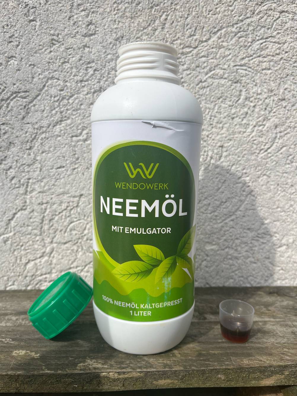 Eine geöffnete Flasche Neemöl steht getestet zwischen Deckel und gefülltem Dosierbecher.