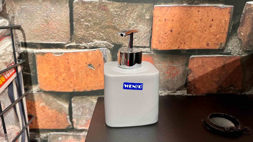 Ein Seifenspender in grau steht zum testen vor einer Wand im Mauerdesign.