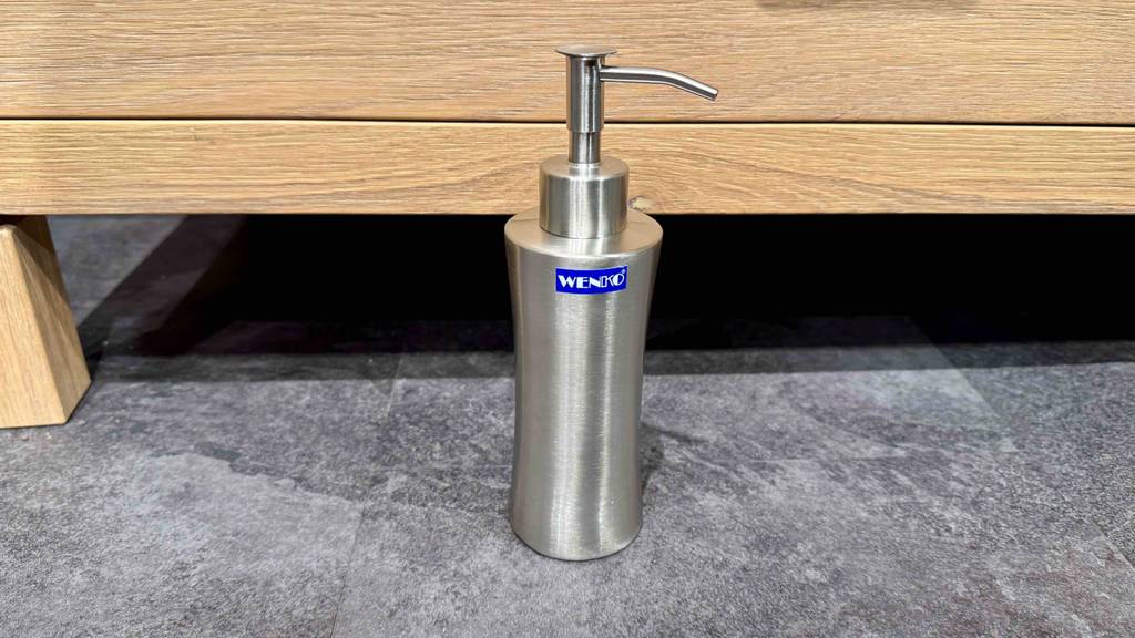 Im Test: Ein Seifenspender aus Edelstahl steht auf dem Boden vor einem Holzregal.