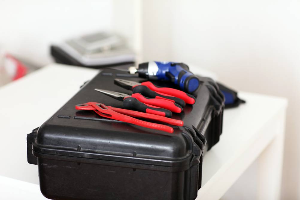 Werkzeugkoffer mit Akkuschrauber im Test: drei Zangen und ein Akkuschrauber liegen auf einem schwarzen Kunststoffkoffer, der auf einem weißen Tisch liegt.