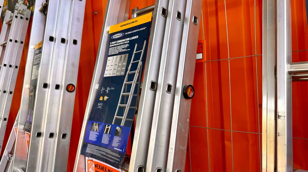 Mehrzweckleitern im Test: Seitenansicht von einigen Modellen, die an einer orangen Wand lehnen.