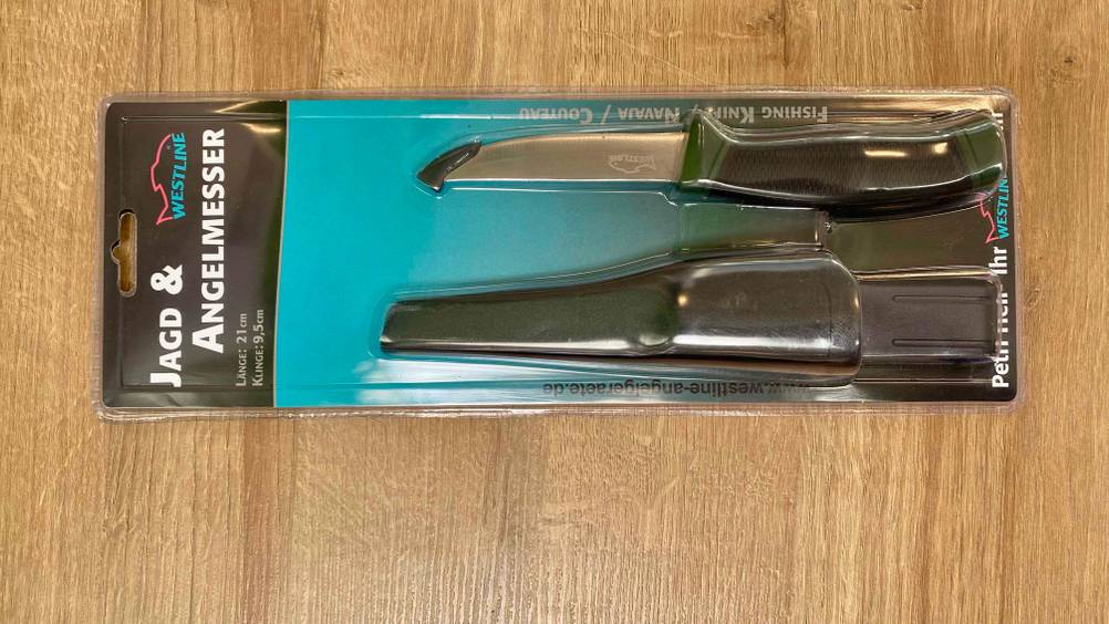 Im Test: Ein originalverpacktes Jagdmesser liegt horizontal auf einer Holzfläche.
