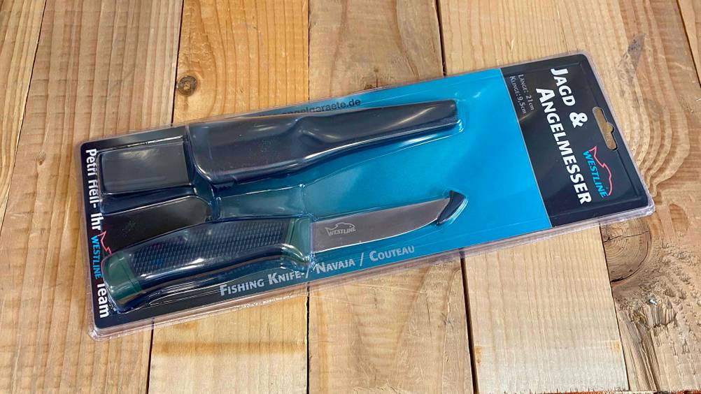 Ein getestetes Jagdmesser in seiner Originalverpackung auf einer Holzfläche.