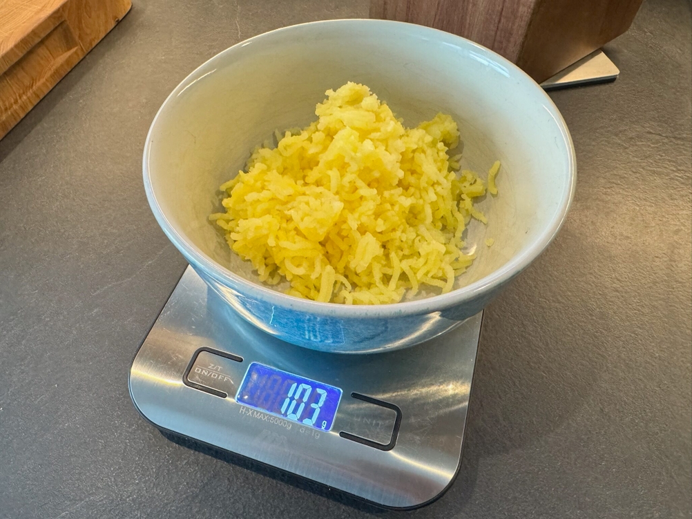 Fertig gepresste Kartoffeln in einer Schale auf einer Waage, auf der 103 g steht.