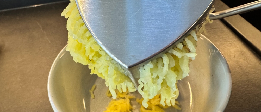 Eine Kartoffelpresse presst feine Fäden direkt in eine Schale.