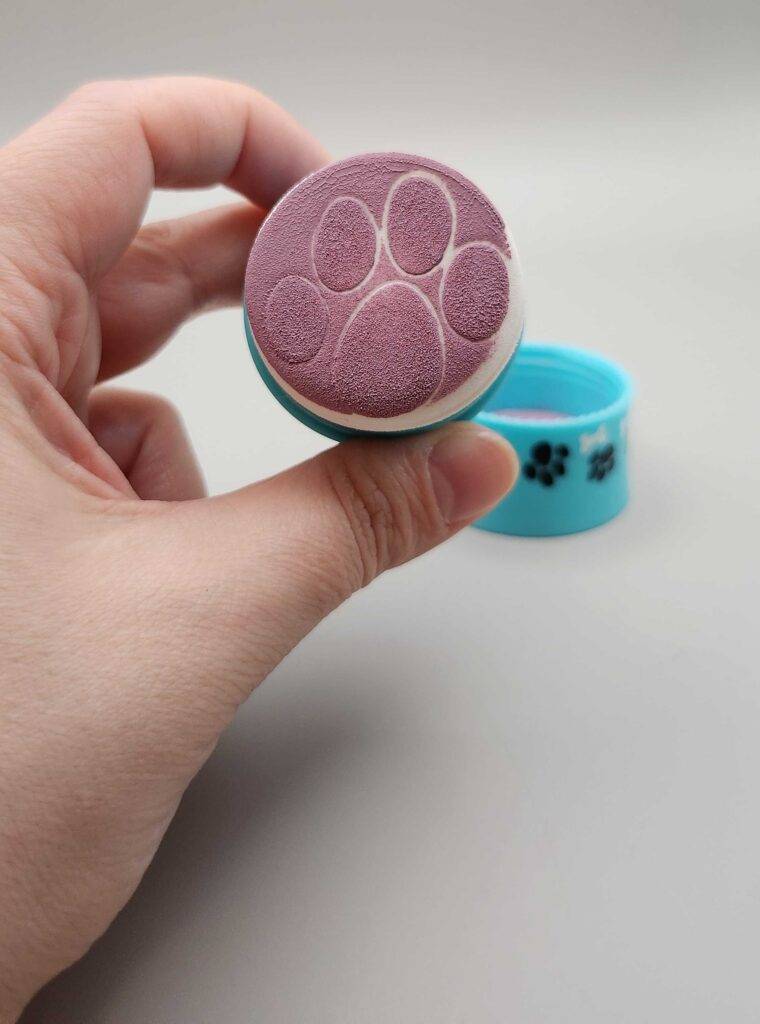 Eine Hand hält den Schwamm einer Dose mit getesteter Creme Rouge vor einem weißen Hintergrund.