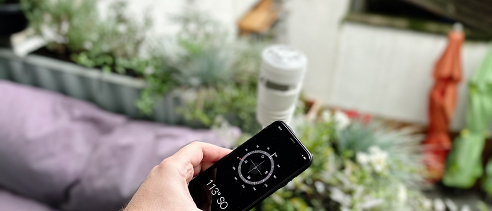 Ein Smartphone zeigt einen Kompass an. Im Hintergrund ist die Wetterstation von Ecowitt zu sehen.