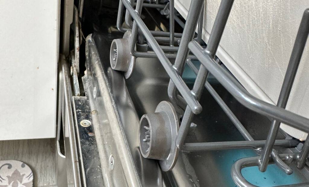Detailansicht von der Seite auf die Transporträder eines Geschirrkorbs, der sich in einem frei stehenden Geschirrspüler im Test befindet.
