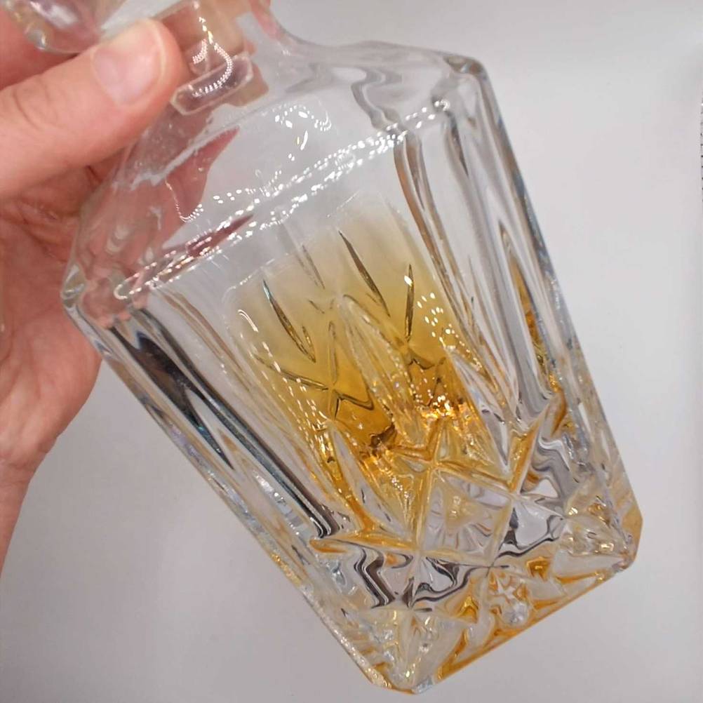 Eine Hand hält den unteren Teil einer Whisky-Karaffe im Test vor eine helle Wand.