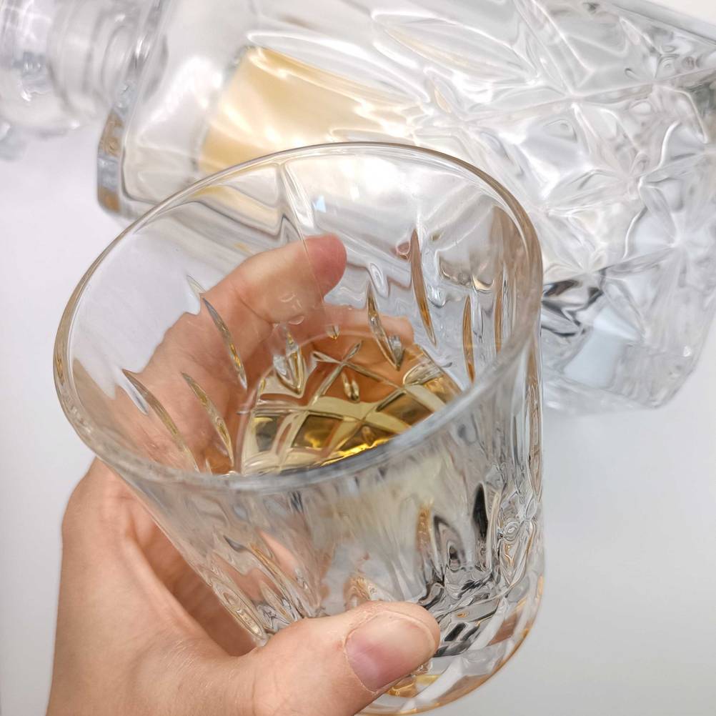 Eine Hand hält ein gefülltes Whiskyglas im Test vor eine Flasche.