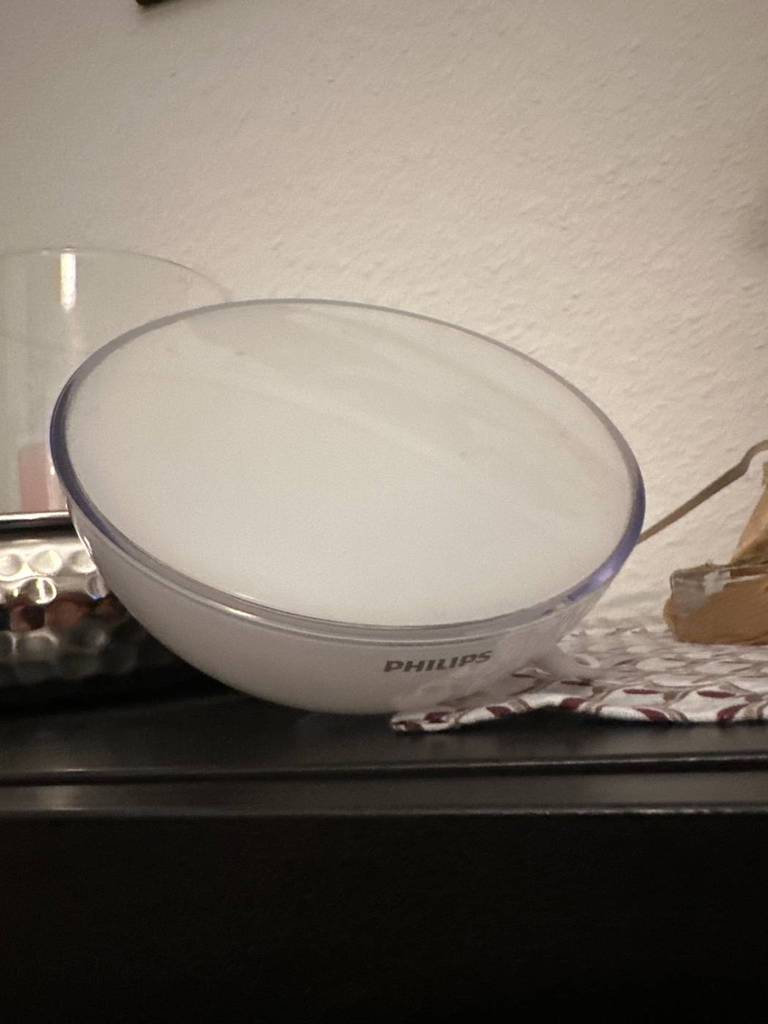 Getestete Tageslichtlampe von Philips liegt mit anderen Gegenständen auf einer dunklen Ablagefläche.