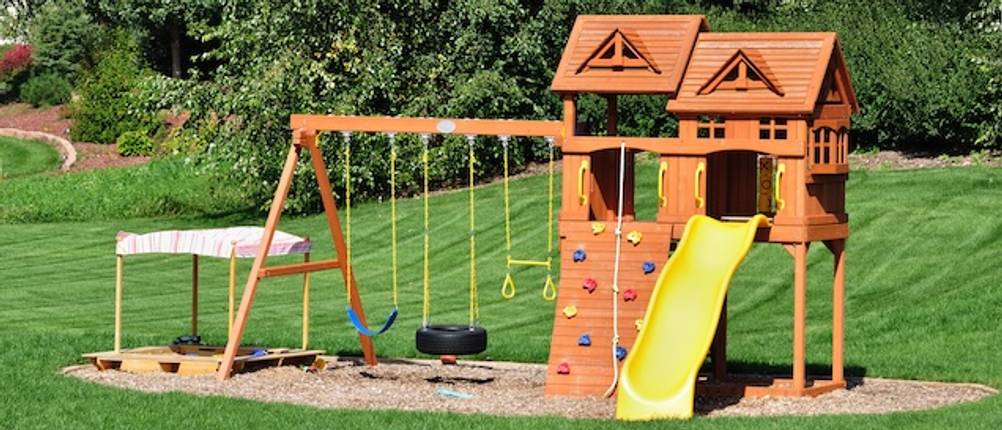 Wickey-Spielturm getestet: Ein Holz-Spielturm mit einer Kletterwand, einer Rutsche und Schaukeln auf einer Grünfläche.