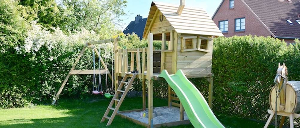 Wickey-Spielturm im Test: Ein Spielturm aus Holz mit einer grünen Rutsche in einem Garten.