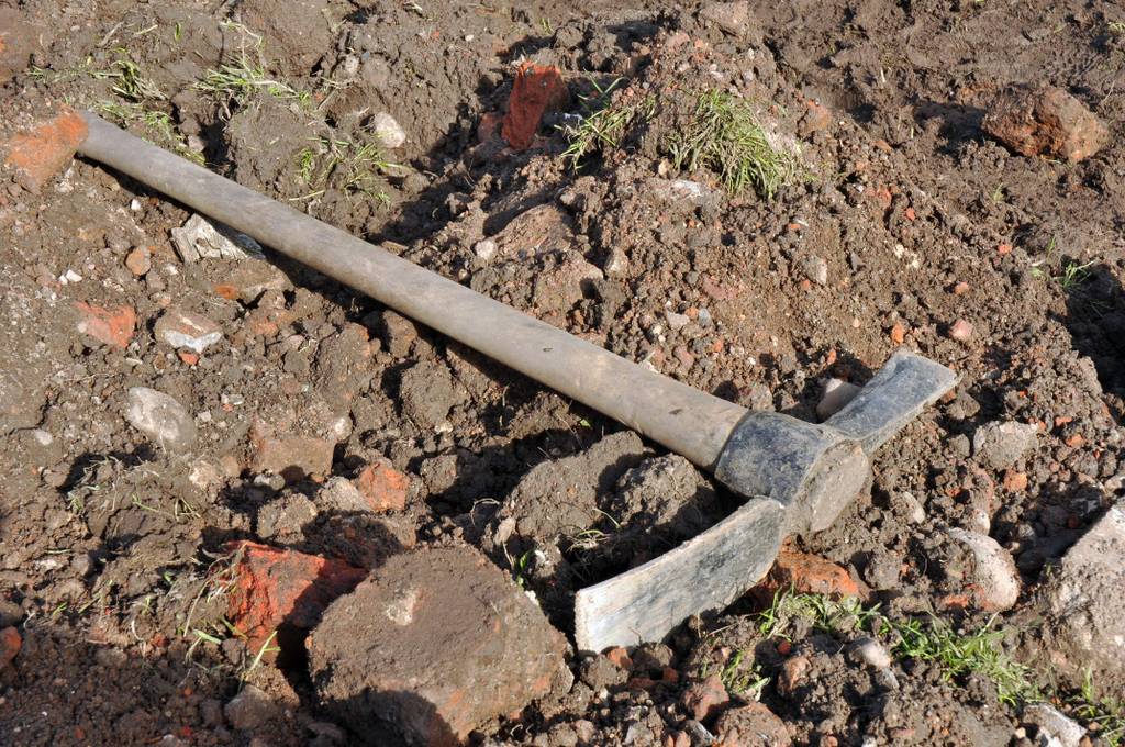 Wiedehopfhacke im Test: Eine Wiedehopfhacke liegt auf offenem Boden der einige Steine und Bruchstücke von Ziegelsteinen zu sehen sind.