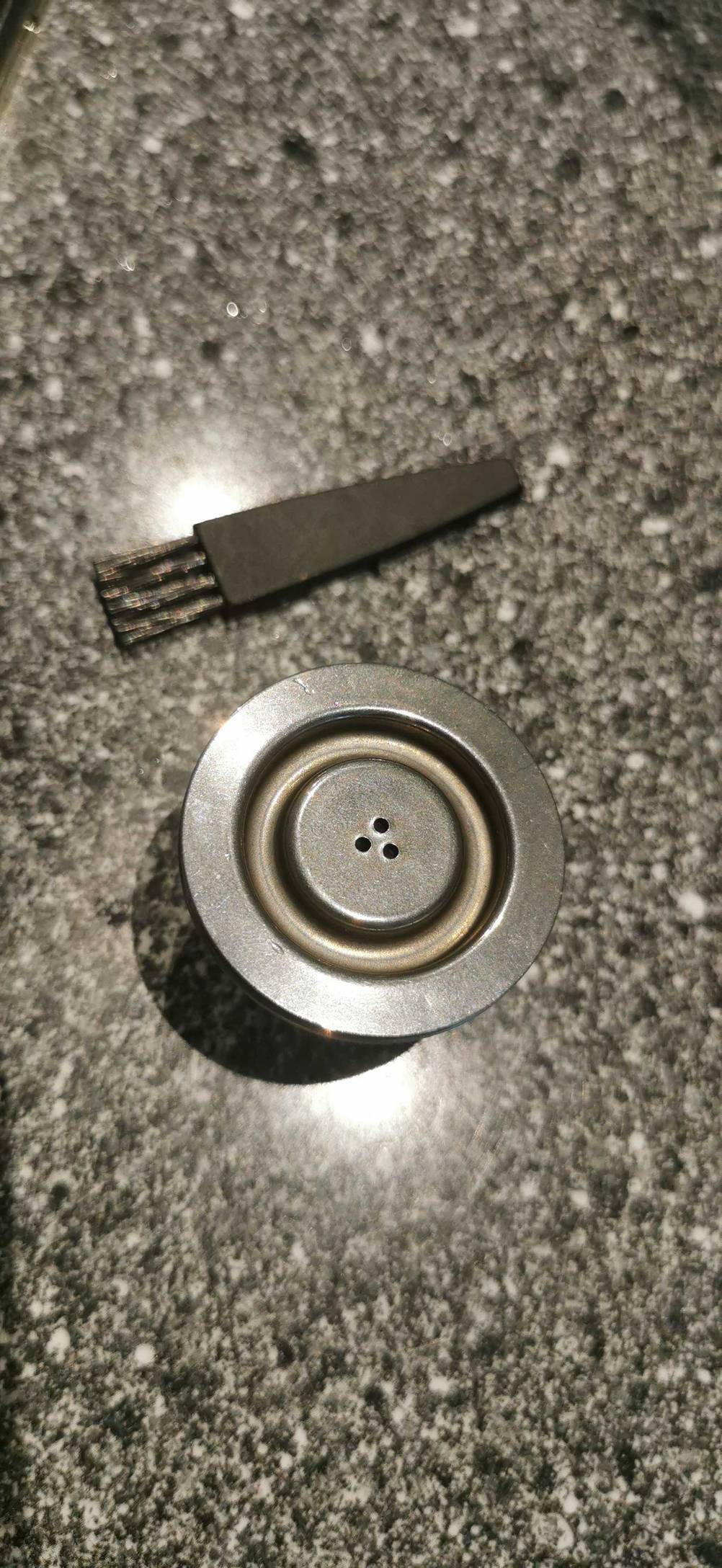 Wiederverwendbare Kaffeekapsel-Test: über einer geschlossenen Kapsel liegt quer ein Pinsel.