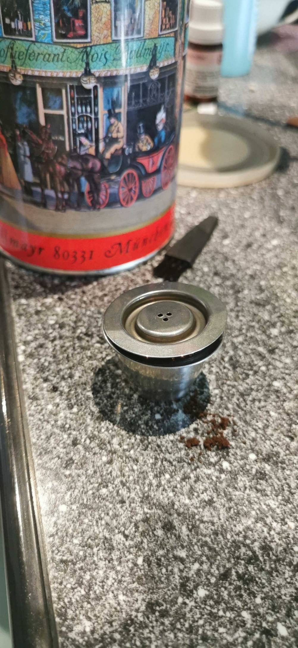 Getestet: Eine gefüllte wiederverwendbare Kaffeekapsel steht auf einer grau gesprenkelten Arbeitsfläche.