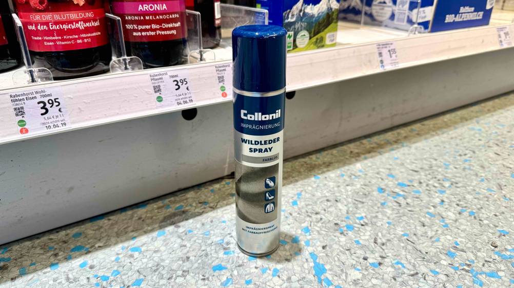Vor einem Verkaufsregal mit Preisangaben steht ein Wildlederspray im Test auf dem Boden.