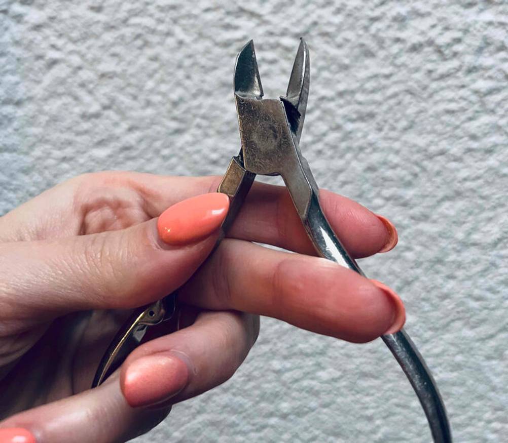 Eine Hand klappt eine Nagelhautzange zum testen auseinander.