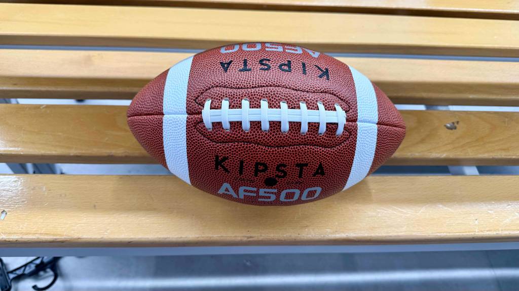 Football-Test: Ein rotes Modell AF500 von KIPSTA liegt auf einer Holzbank.