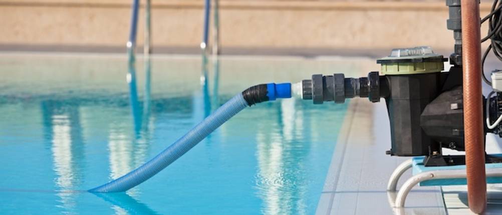 WilTec-Poolpumpen-Test: Eine Poolpumpe neben einem Pool mit einem Schlauch, der von der Pumpe in den Pool führt.