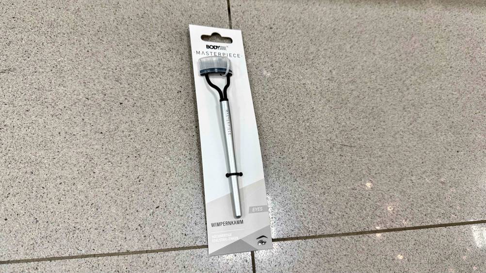 Auf dem Fließenboden liegt ein verpackter Wimpernkamm im Test.