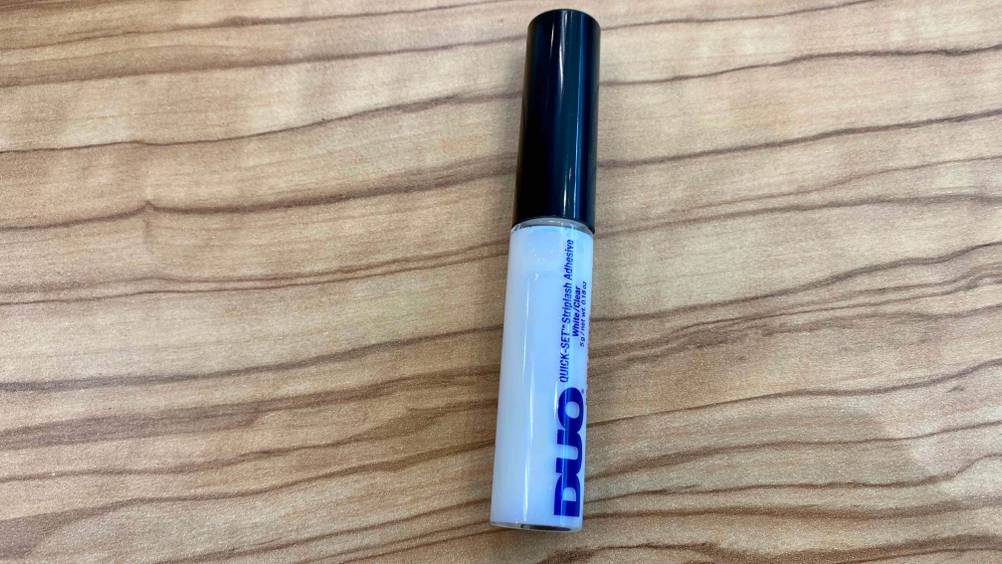 Ein Fläschchen Wimpernkleber im Test leicht seitlich auf einer Holzfläche.