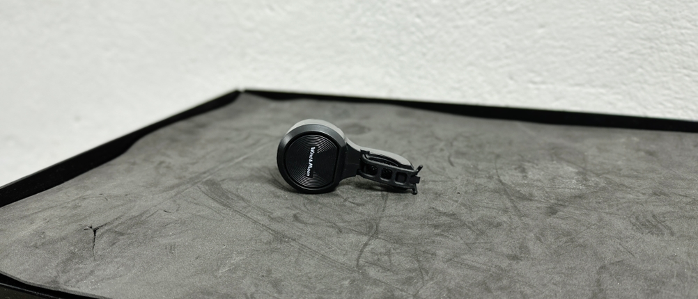 Die Wind&Moon-Fahrradklingel liegt auf einer schwarzen Oberfläche. Ihr kompaktes, rundes Design mit schwarzer Befestigung ist gut zu erkennen.