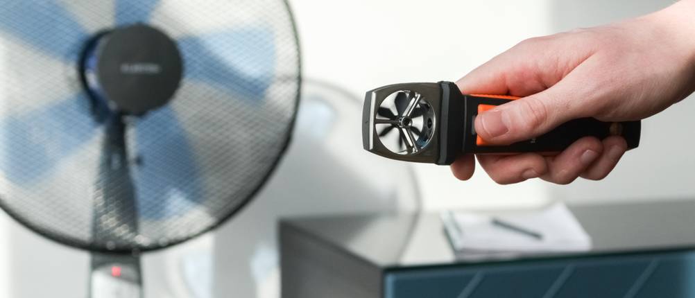 Mit einem Anemometer wird der Luftstrom eines Standventilators gemessen.