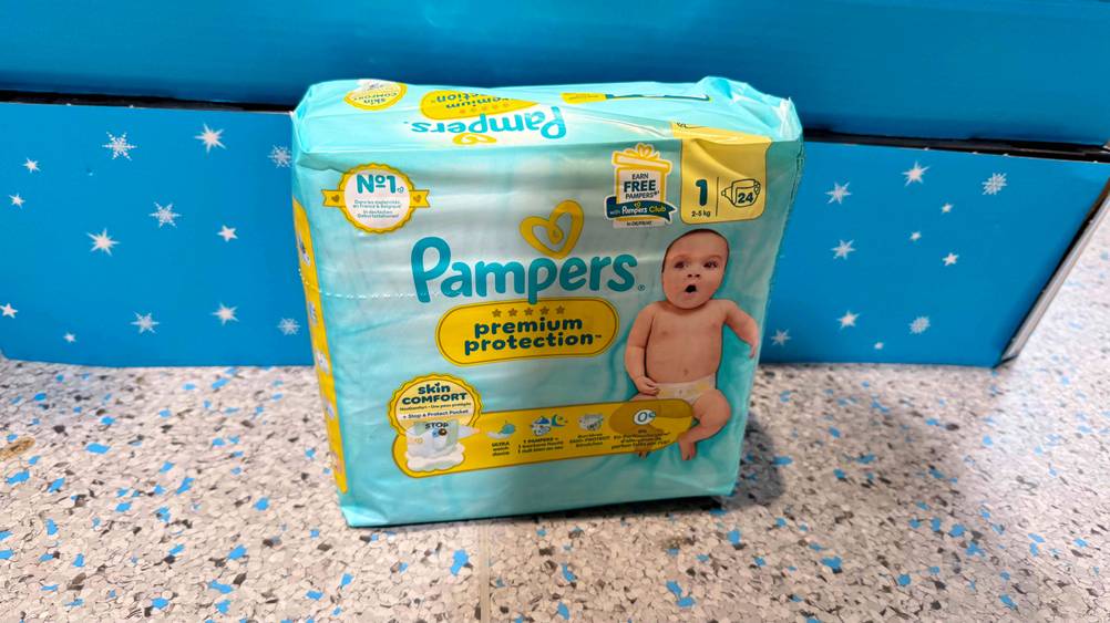Eine Packung der getesteten Windeln Größe 1 stehen vor einem blauen Karton auf dem Boden.