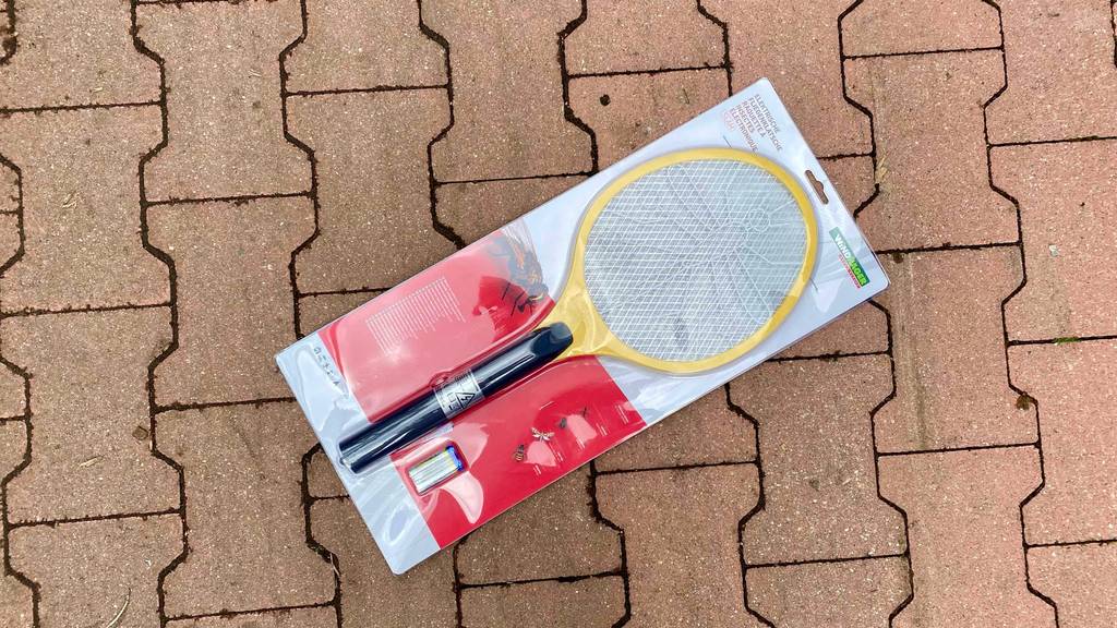 Eine elektrische Fliegenklappe im Test inklusive Batterien eingeschweißt in einer weiß-roten Verpackung auf Terrakotta-Pflastersteinen.