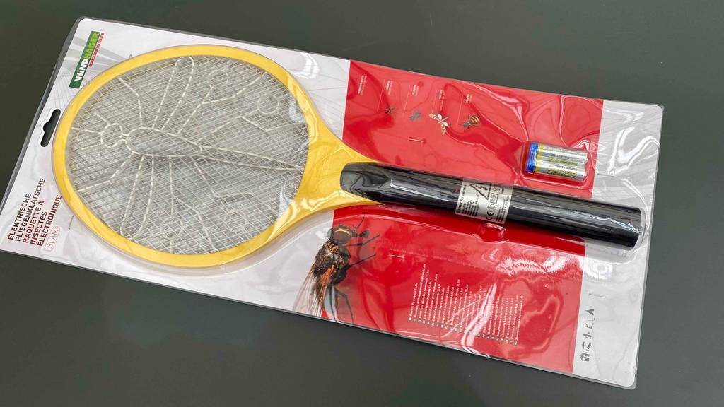 Eine elektrische Fliegenklappe im Test liegt eingeschweißt in ihrer weiß-roten Verpackung auf einem schwarzen Untergrund.