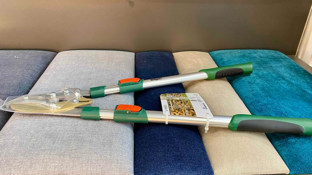 Im Test: Eine Teleskop-Heckenschere von der Seite auf einem Polstermöbel liegend.