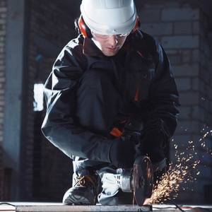 Arbeiter mit Schutzhelm bedient einen Winkelschleifer.