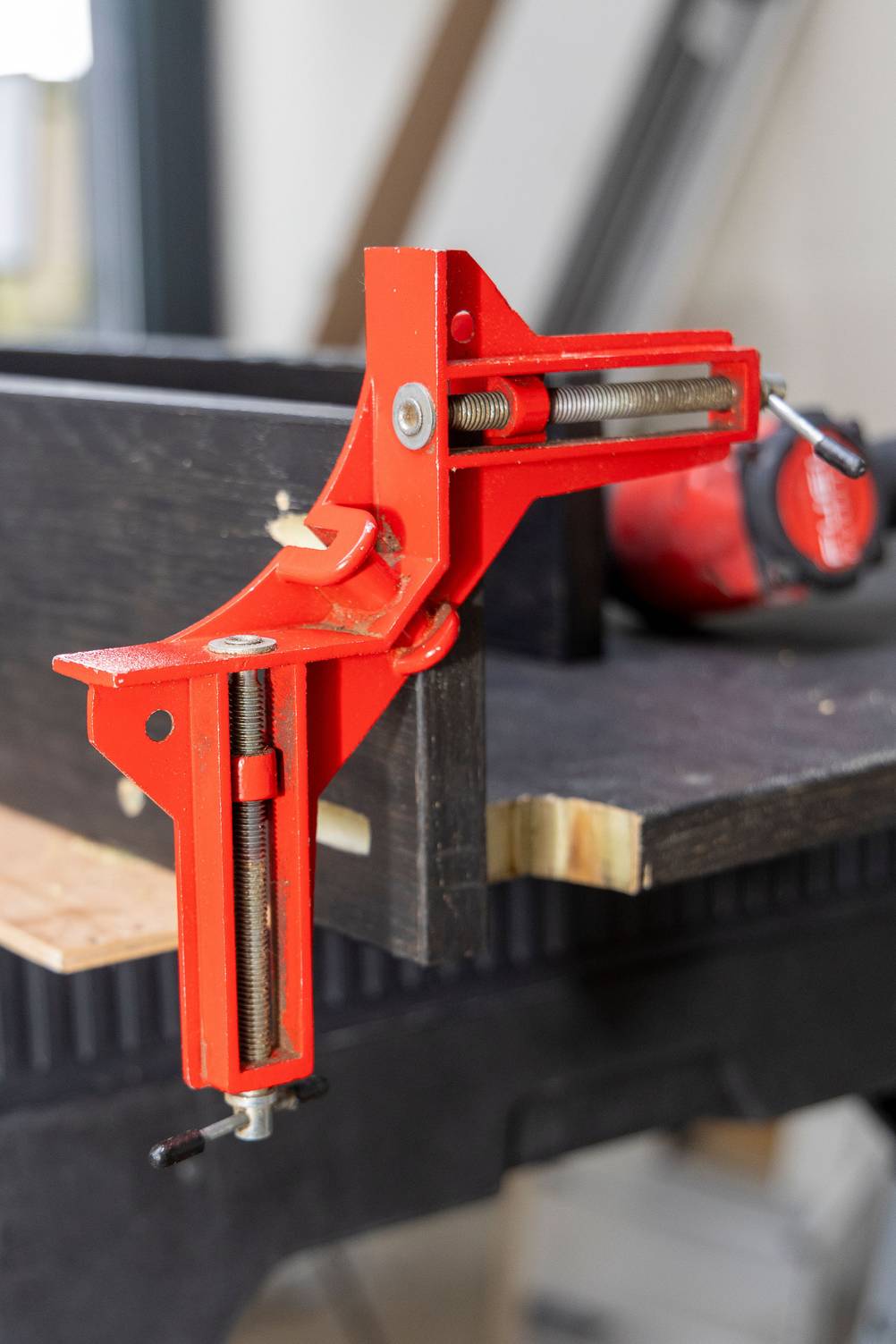 Winkelspanner im Test: Ein rot lackierter Winkelspanner an einem Holzwerkstück aus dunklem Holz.