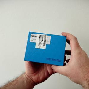 Eine Person hält die blaue Verpackung des Winnes TK913 in beiden Händen. Der Karton ist mit einem Versandetikett versehen.