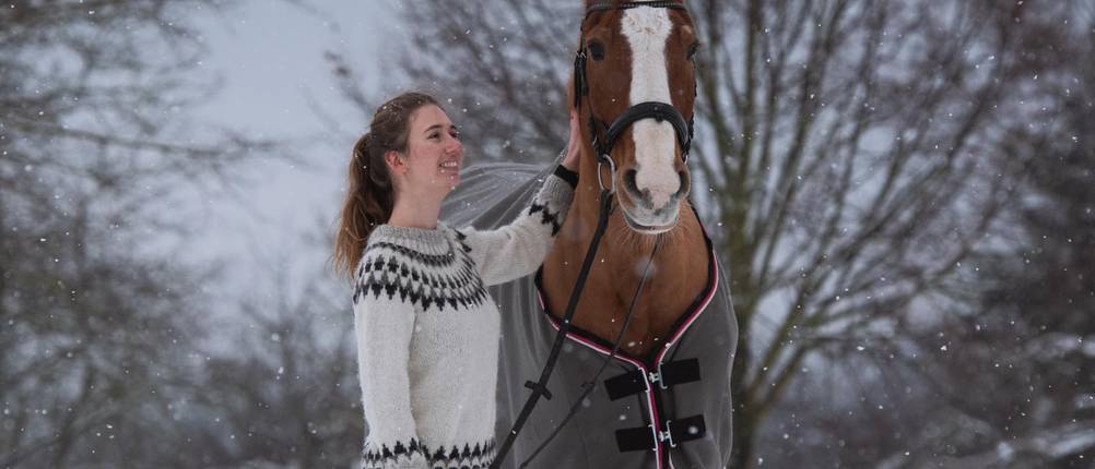 Winterdecke-Pferd-Test: Eine Frau steht im Winter mit einem großen Pferd mit Winter-Pferdedecke draußen auf der Koppel.