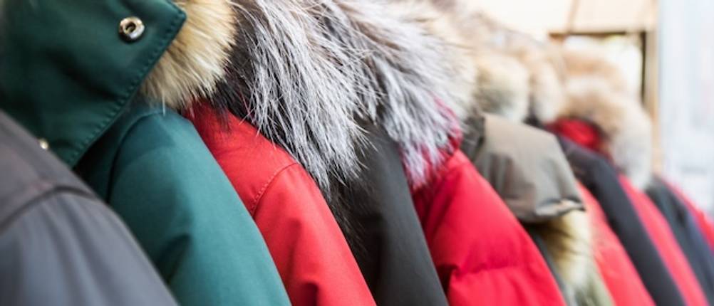 Damen-Winterjacken im Test: Auf einer Kleiderstange hängen verschiedenfarbige Damenjacken mit Kunstpelzkragen.