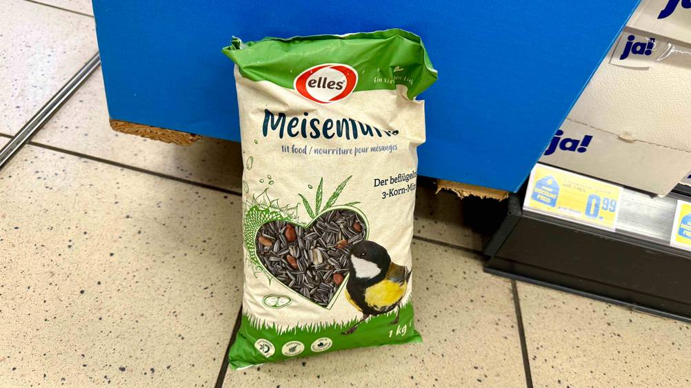 Auf einem Fließenboden lehnt eine Packung des Wintervogelfutters im Test an einer blauen Box.