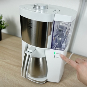 Eine Hand drückt die Einschalttaste der Melitta Look V Perfection. Die grüne Betriebsleuchte ist aktiv.