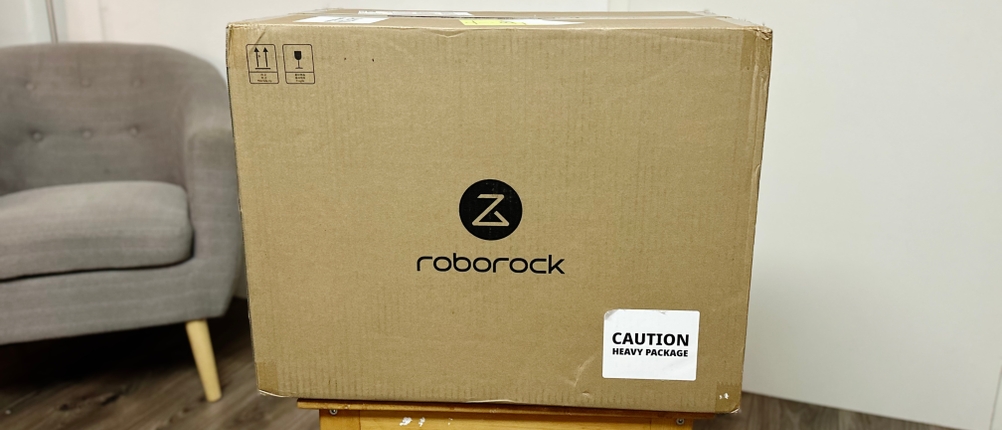Die Verpackung des Roborock-Wischroboters steht auf einem Holzhocker.