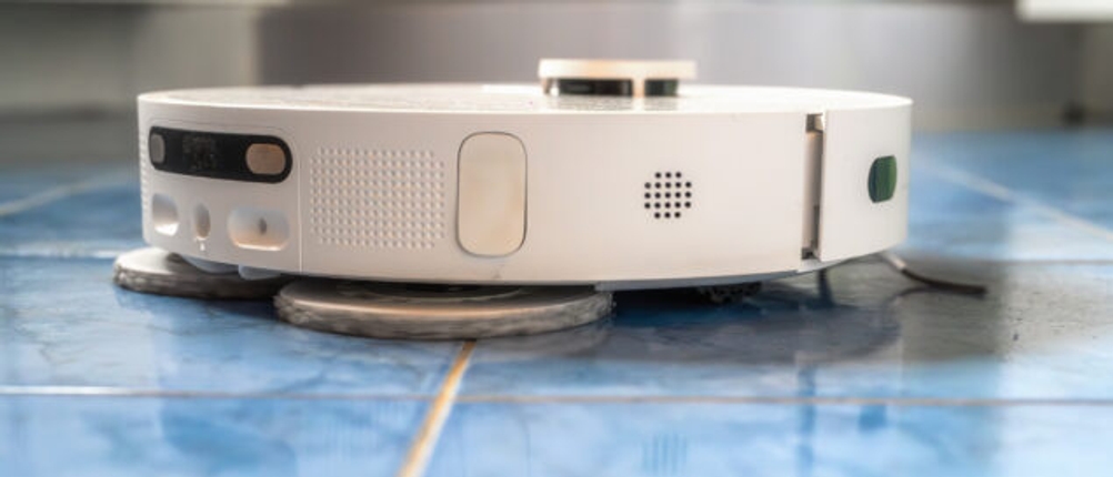 Ein weißer Wischroboter wischt hellblaue Fliesen in einem Badezimmer.