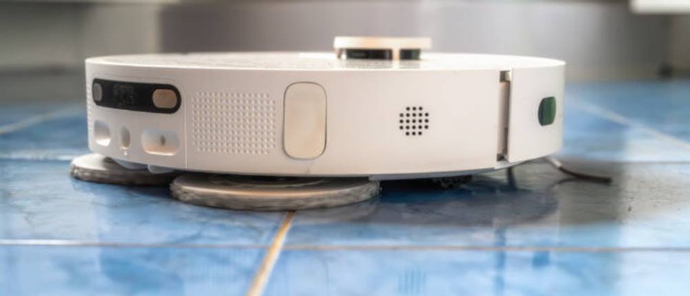 Ein weißer Wischroboter wischt hellblaue Fliesen in einem Badezimmer.