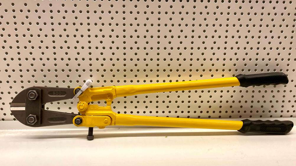 Ein getesteter Bolzenschneider lehnt an einem weißen Lochblech.