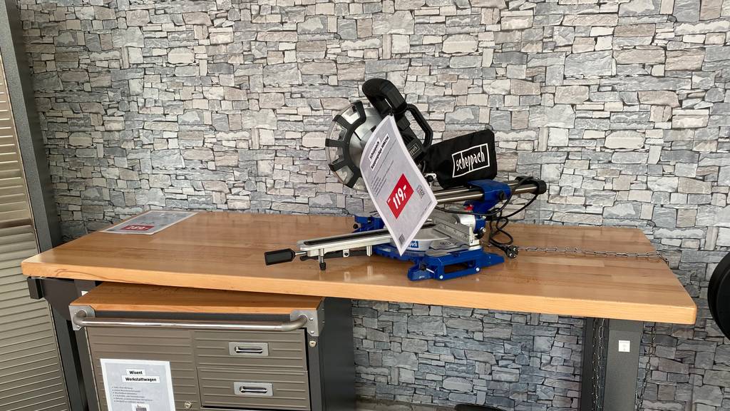Übersichtliche Ansicht einer stehenden getesteten Holz-Werkbank, auf der ein Winkelschneider steht und unter der sich ein Werkstattschrank befindet.
