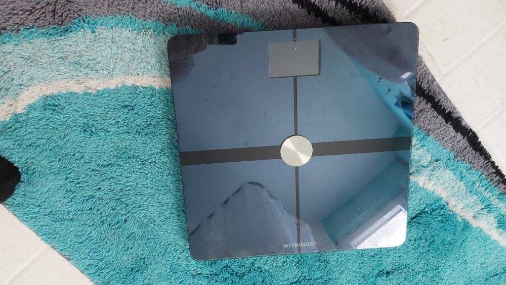 Im Test: schwarz glänzende Körperfettwaage von Withings steht ausgeschaltet auf einem türkisfarbenen Badvorleger.