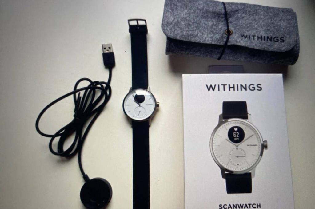 EKG-Uhr-Test: Withings-Modells mit weiß-schwarzem Ziffernblatt und schwarzem Armband liegt neben der Originalverpackung sowie dem Zubehör auf weißem Untergrund.