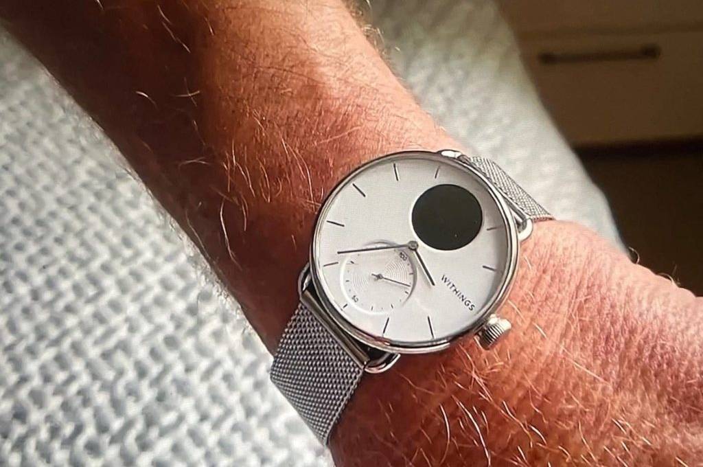 EKG-Uhr im Test: Nahaufnahme eines eleganten Withings-Modells mit weiß-schwarzem Ziffernblatt inklusive Edelstahl-Armband an einem männlichen Handgelenk vor weißem Stoff.