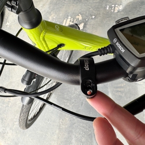 Eine Hand hält die Halterung des Wittkop 89010030 an einen Fahrradlenker.